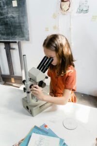 A curious young girl examines a specimen with a microscope in a classroom setting.